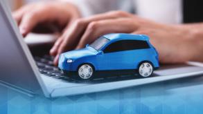 Person using a laptop, with a blue toy car sitting on top. 