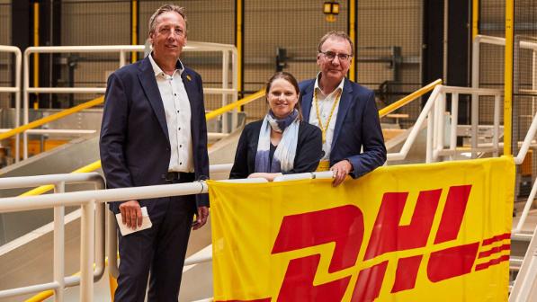 Drei DHL-Führungskräfte stehen hinter einem DHL Banner