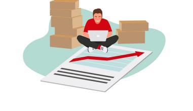 Man sitting on the floor among boxes and a flipchart working on his computer.
