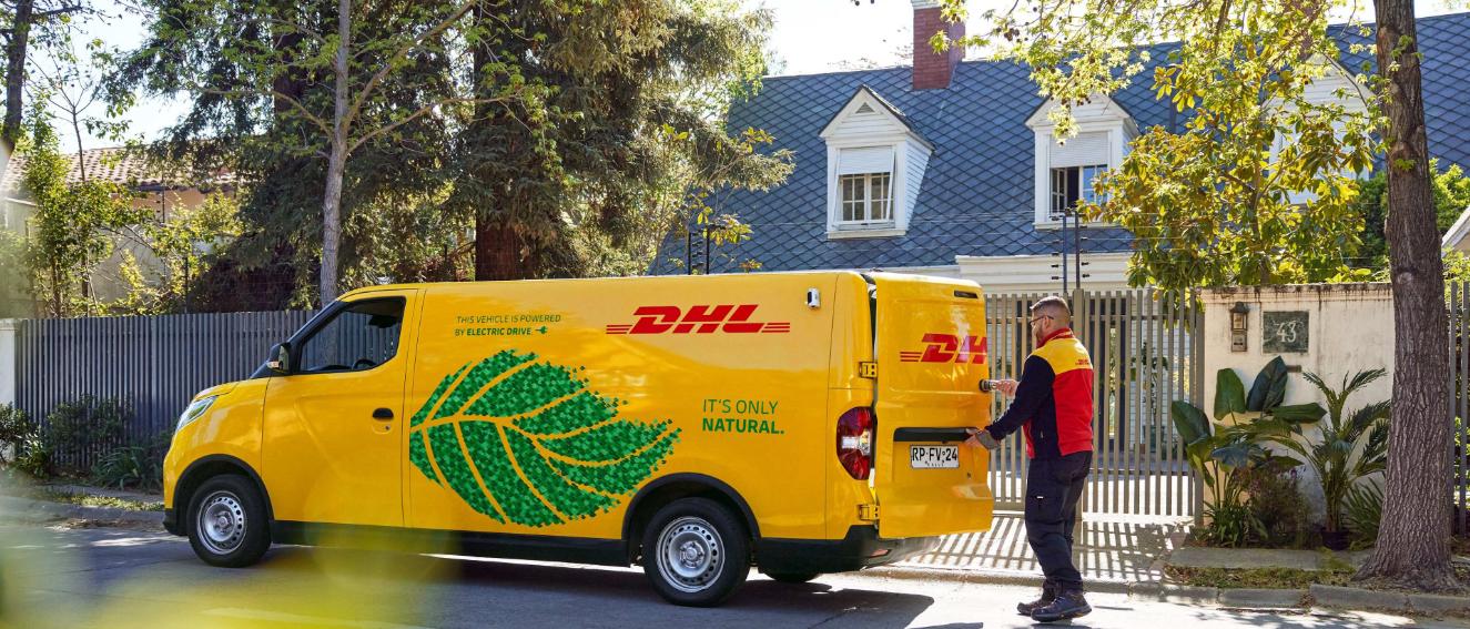 Electric DHL delivery van outside a gated home with a DHL driver opening the vehicle.