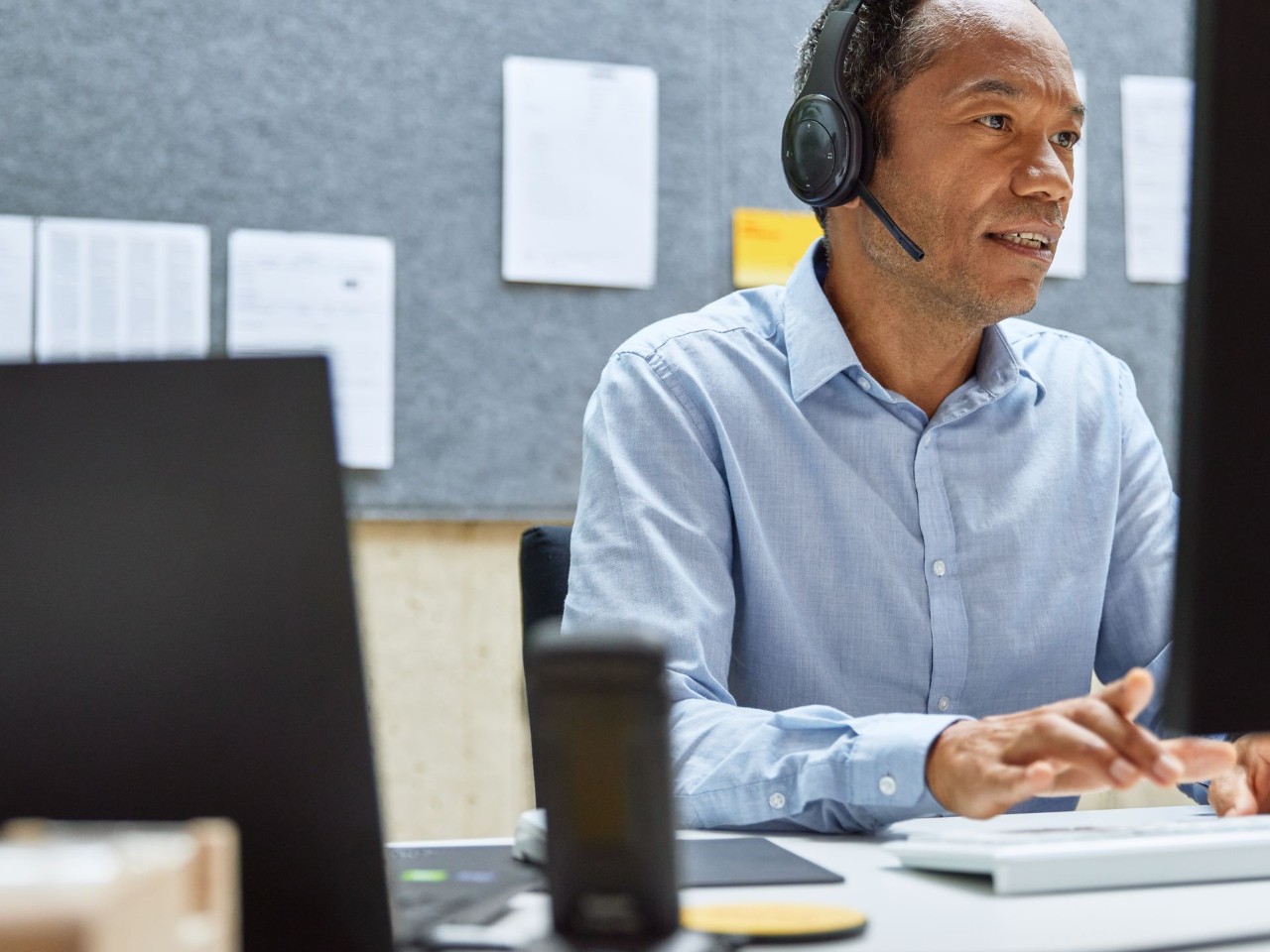 Un hombre que trabaja en la computadora comunicándose con un auricular. 