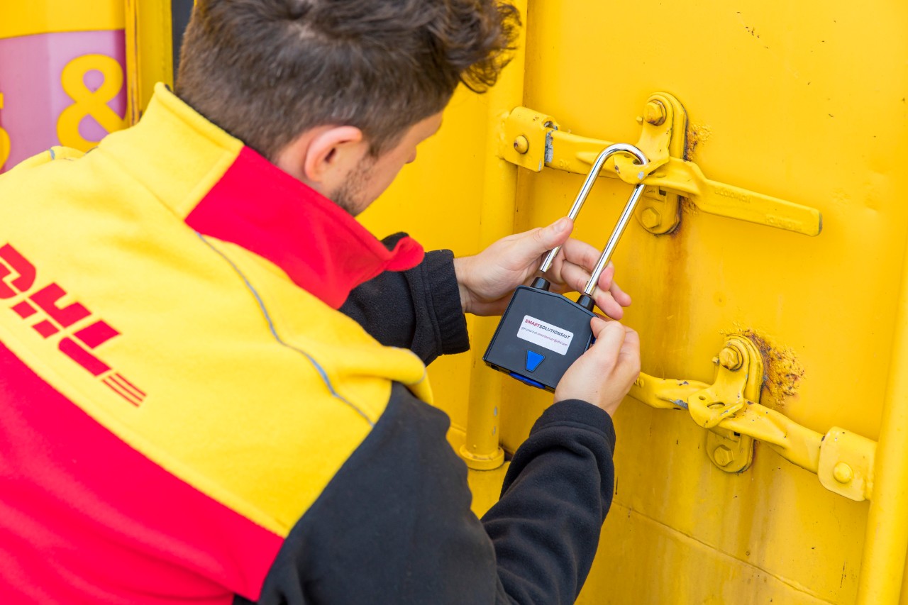 DHL male employee in uniform locking a yellow container by hand. 