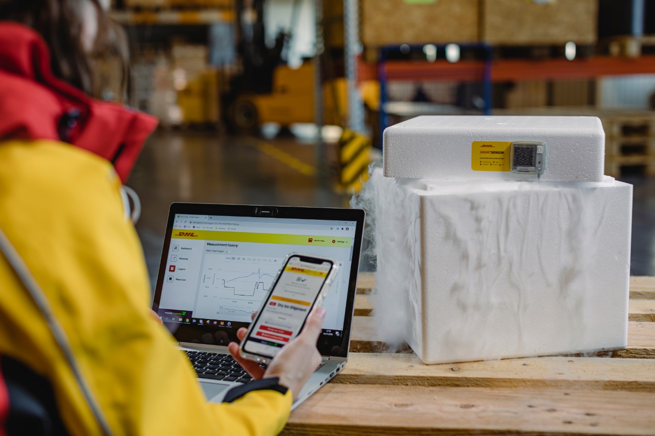 DHL employee working in a warehouse using a laptop and smartphone.