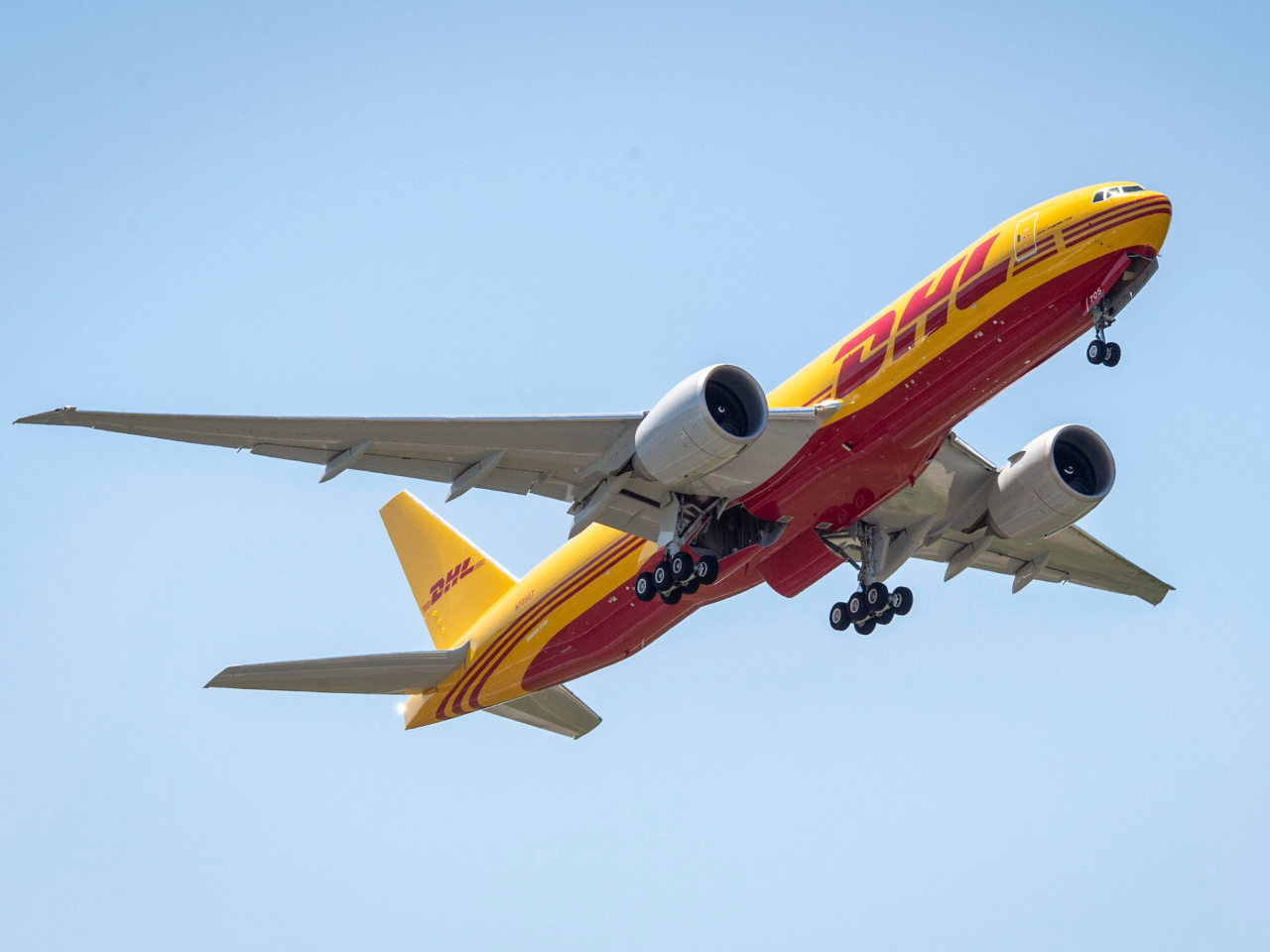 A DHL cargo airplane with a yellow and red livery is shown in flight against a clear blue sky, epitomizing efficient shipping for small businesses.