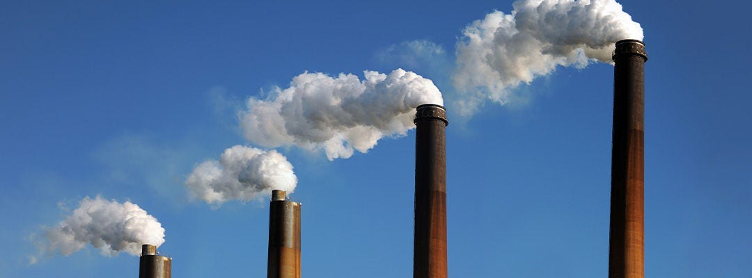 Industrial smokestacks with smoke clouds over blue sky