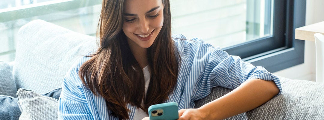 woman in a blue shirt smiling at mobile phone screen