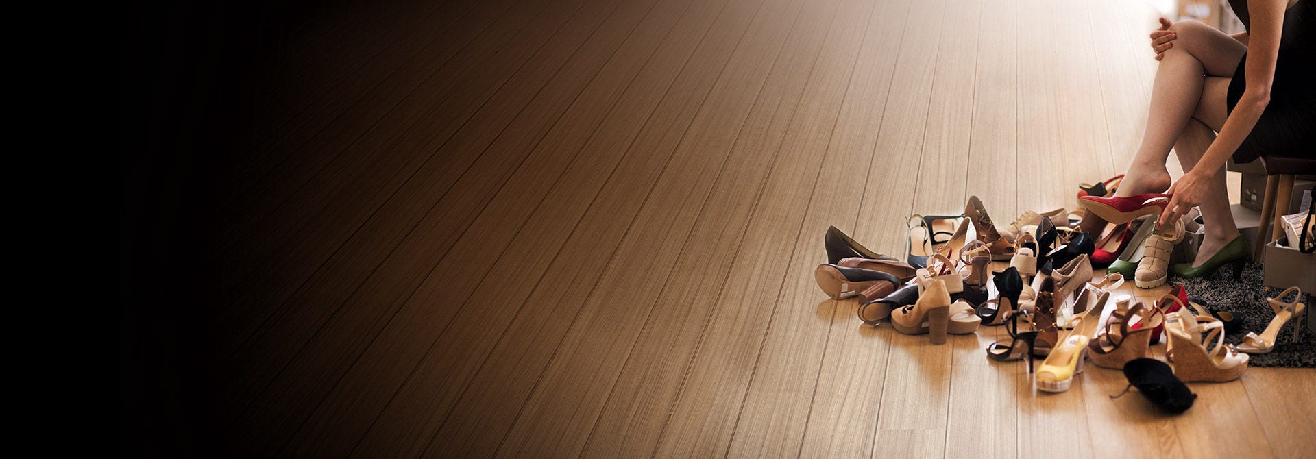 Woman sitting trying on shoes with several pairs around her