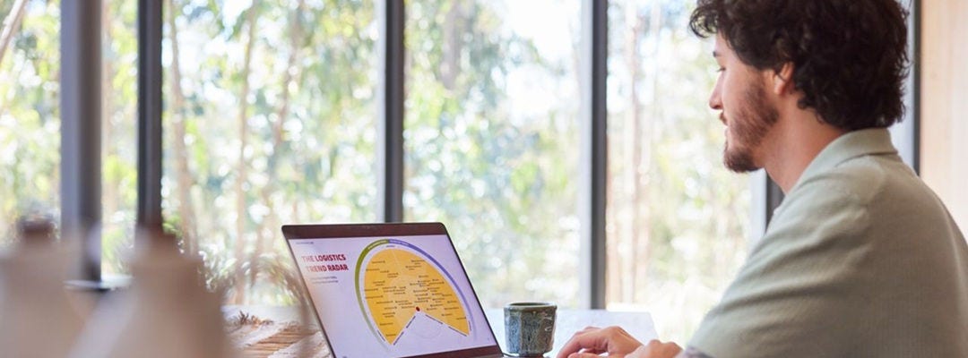 A young man is checking the DHL Trendradar on his laptop at home. His smartphone case and charger are DHL-branded.