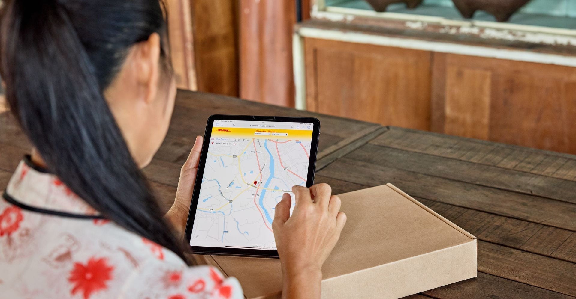 woman tracking DHL package on tablet next to a parcel box