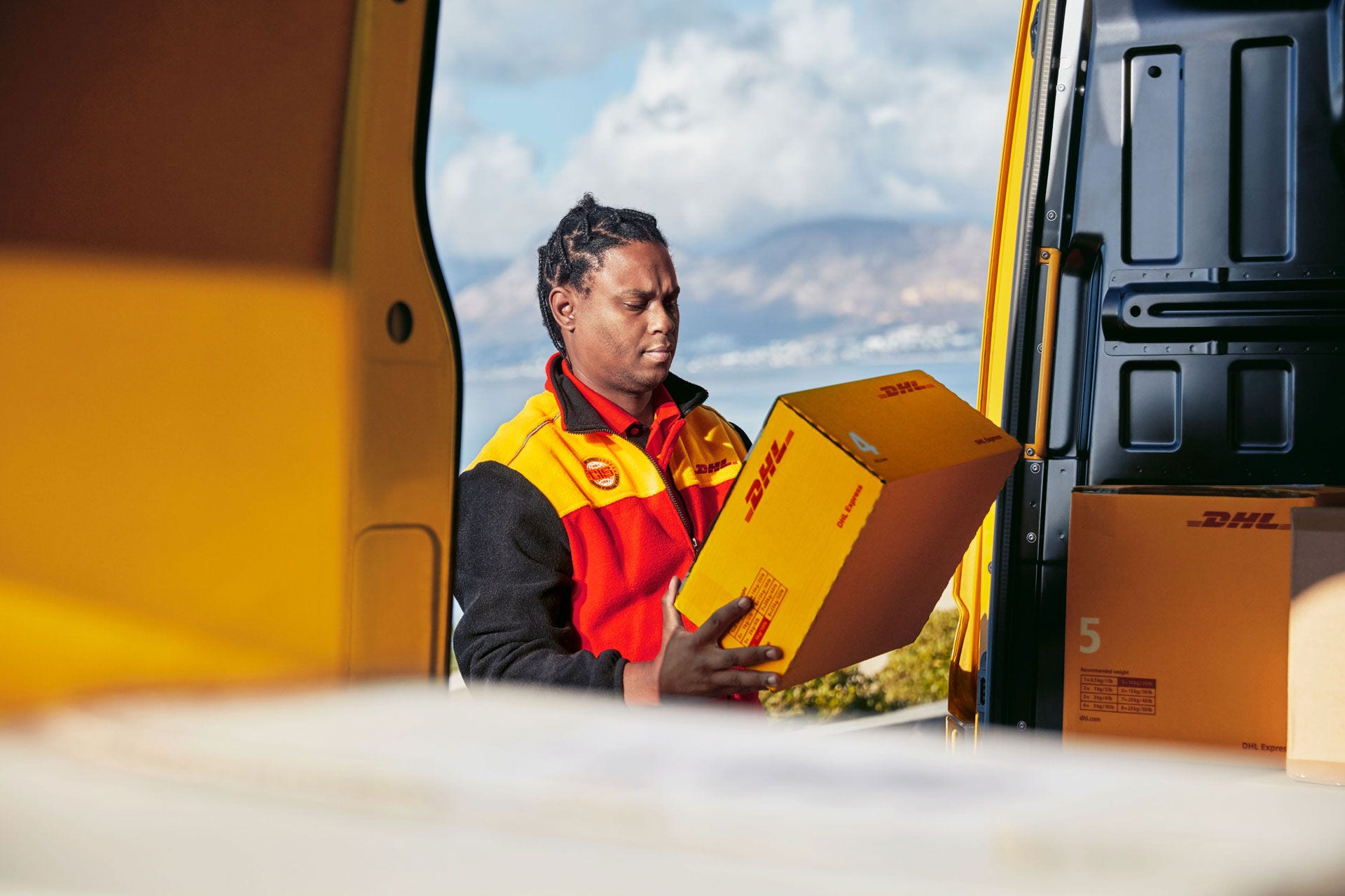 Postman looks at parcel in delivery van, sea view in the background