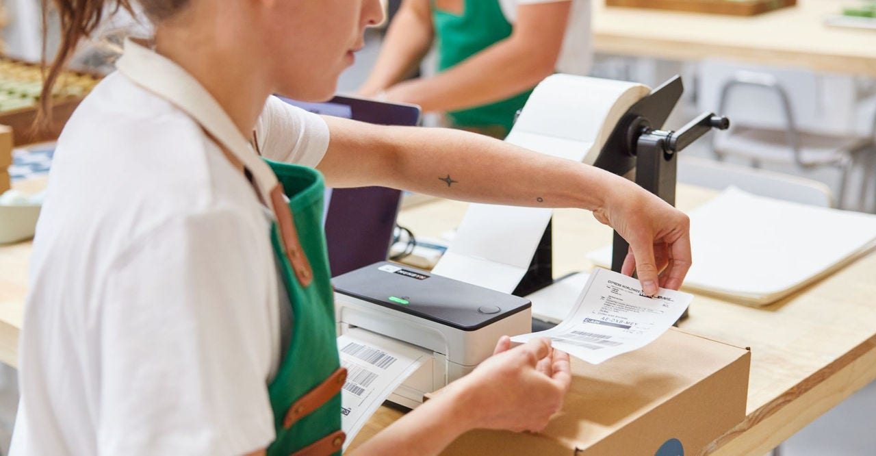 a woman is sticking a bill on a parcel to prepare it for shipping.