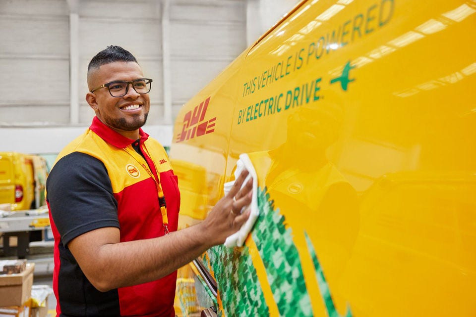 A male DHL employee is cleaning an electric DHL van at a DHL Hub.