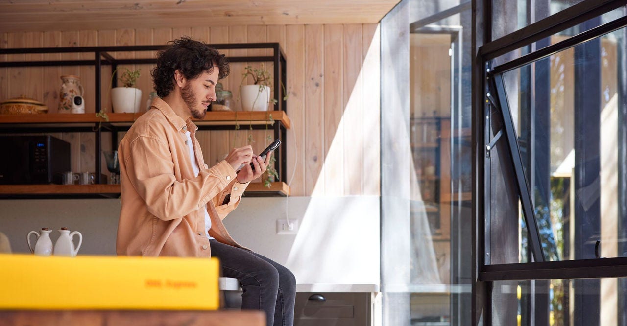 a male sitting on a kitchen counter, holding a smartphone with a dhl express parcel visible in the image