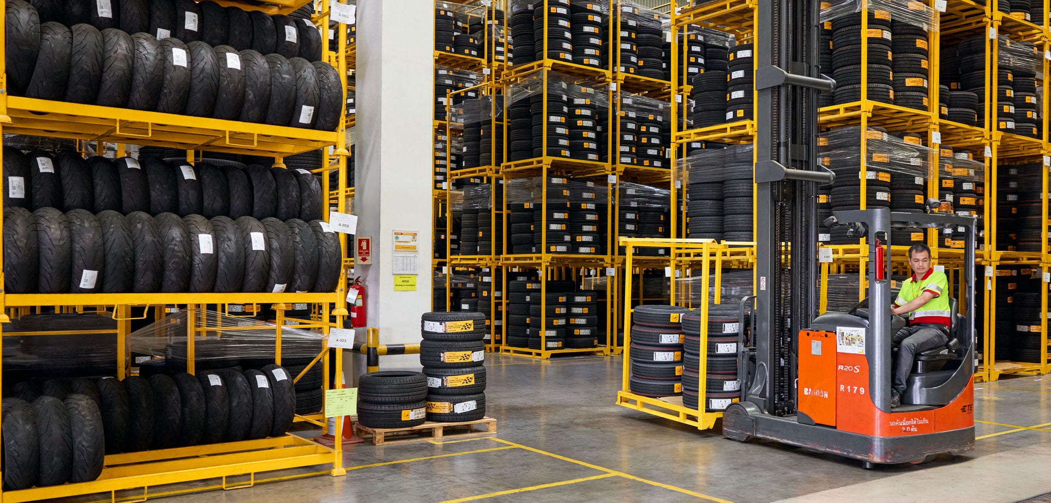 A male DHL employee operates a forklift and stores tires in a high-bay warehouse.