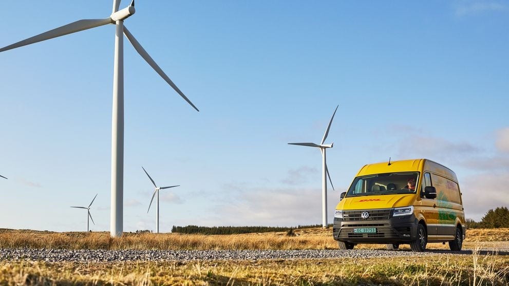 A DHL Express van drives past a field of wind turbines.