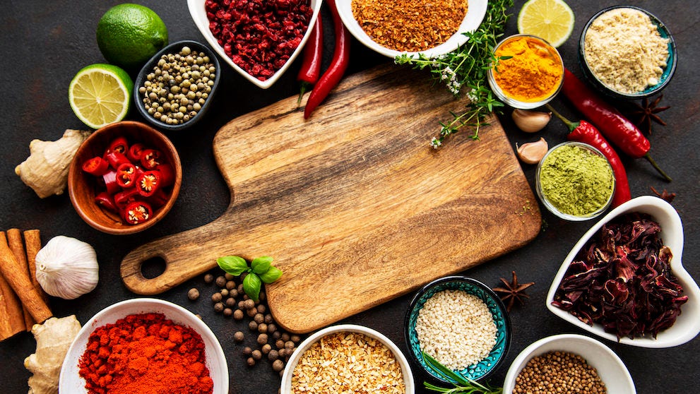 Various spices in a bowls and empty cutting board on black concrete background. Top view copy space.