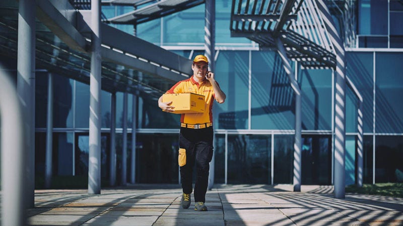 Un coursier DHL livrant un colis tout en parlant sur un portable.