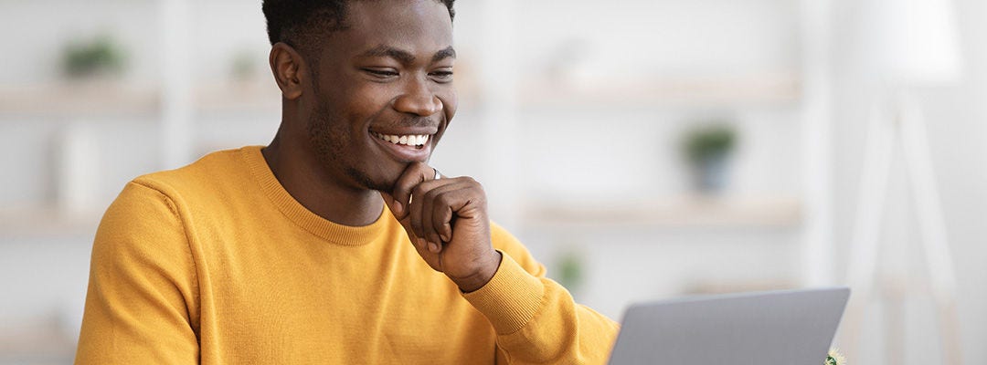 Happy black guy project manager sitting at workdesk at office, typing on laptop keyboard and smiling, chatting with clients, enjoying his job, copy space.