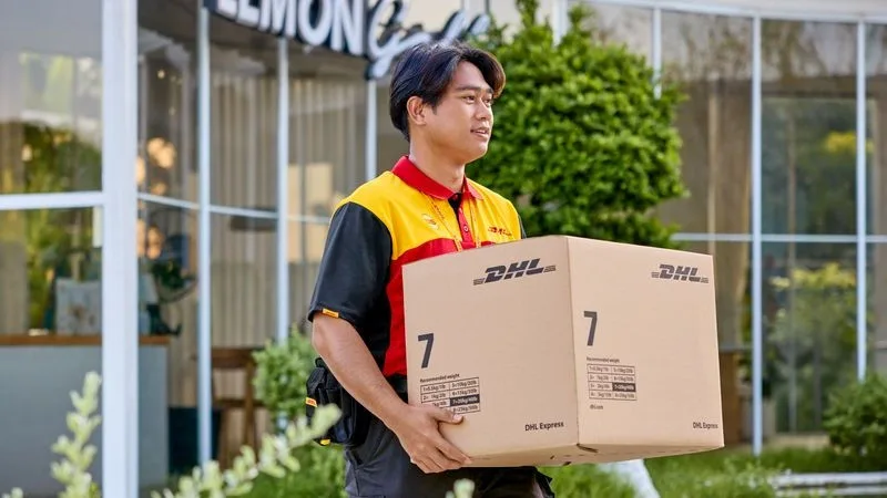 A male DHL employee who just picked up a sustainable brown DHL Express parcel