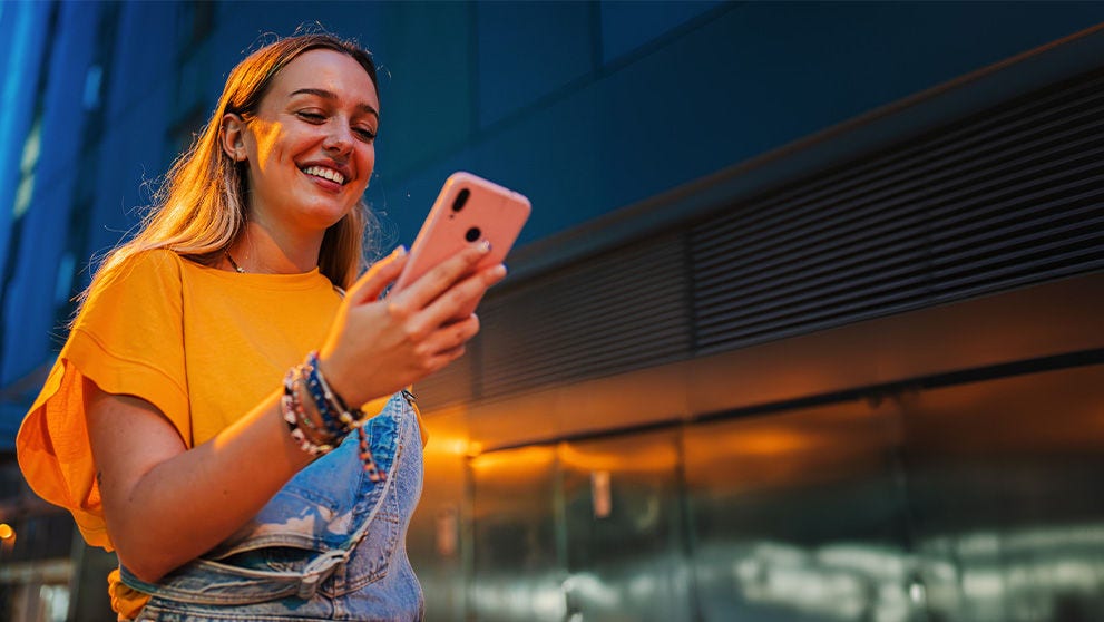 Copy space. One happy young girl using her smartphone to browse the internet while walking on the street at night.