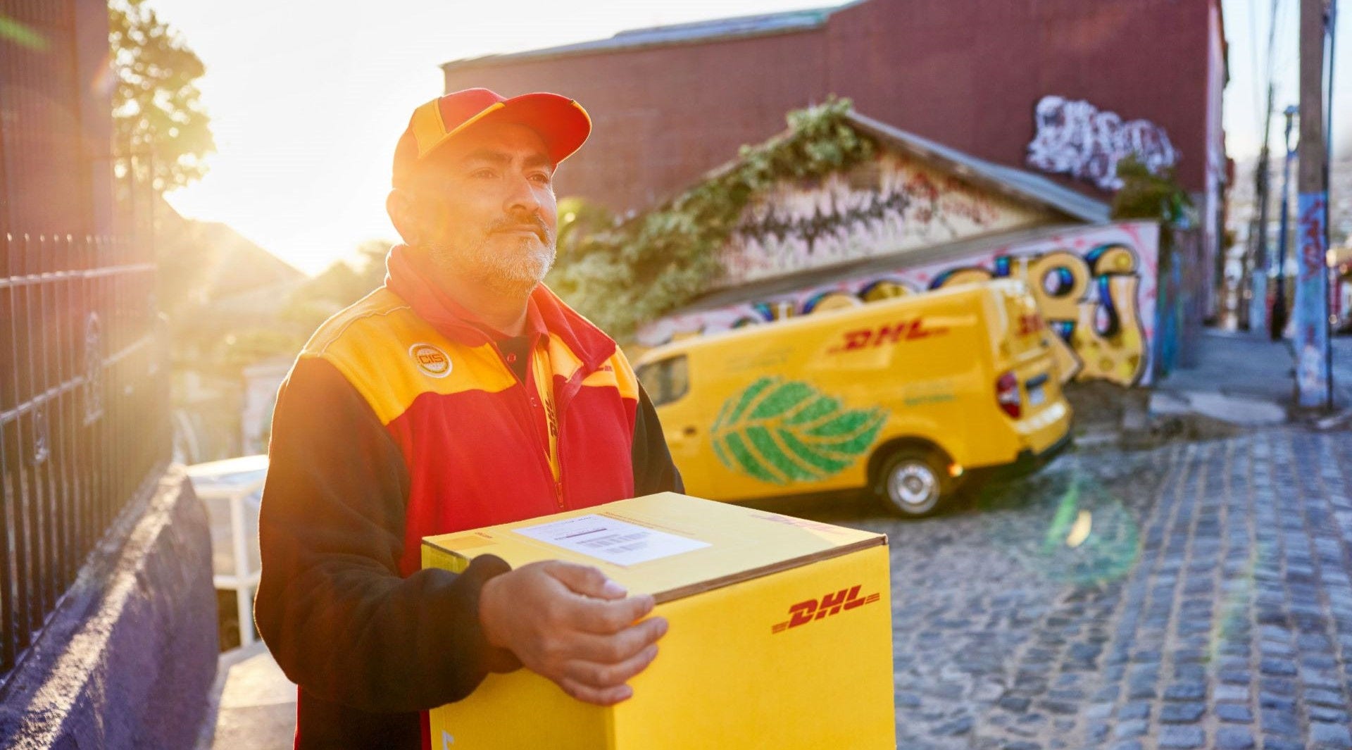 DHL male courier carrying a box against the sunset