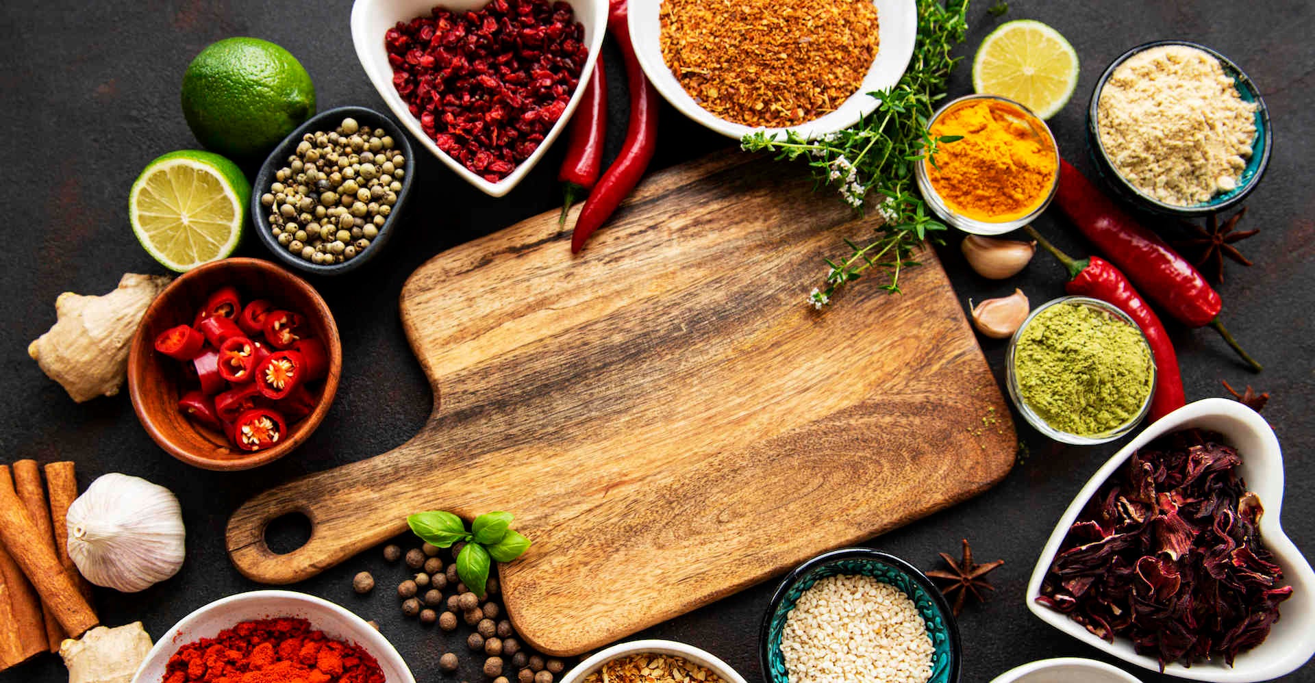 Various spices in a bowls and empty cutting board on black concrete background. Top view copy space.