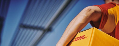 Kurir DHL dengan percaya diri membawa paket kuning bermerek melintasi jembatan modern, melambangkan kecepatan, keandalan, dan konektivitas logistik global. Citra tersebut menyampaikan profesionalisme dan layanan yang efisien dalam pengiriman paket.