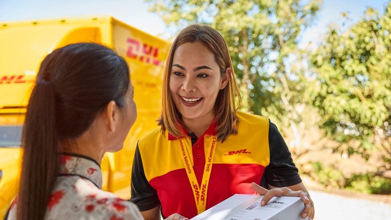A female customer is receiving a parcel from a smiling DHL female employee.