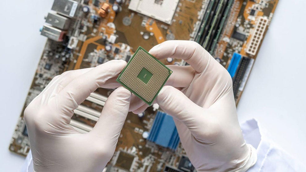a pair of gloved hands holding a cpu chip on top of a motherboard