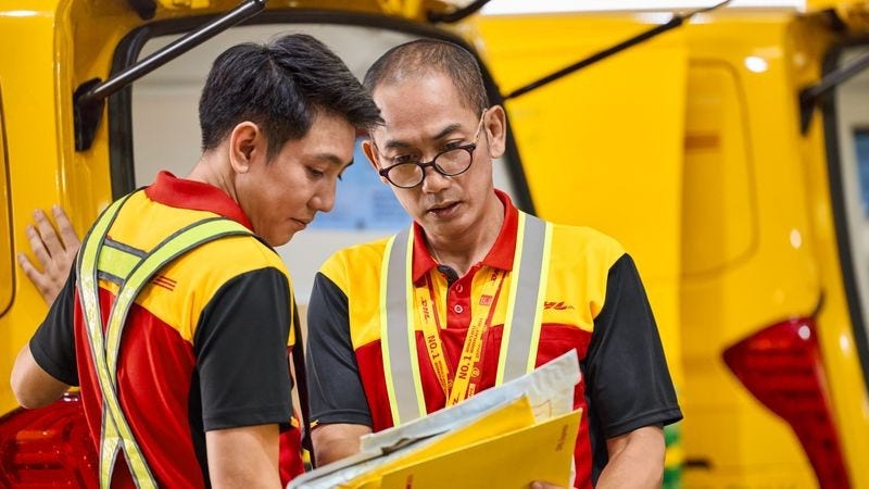 Two DHL employees check the labels of several express envelopes.