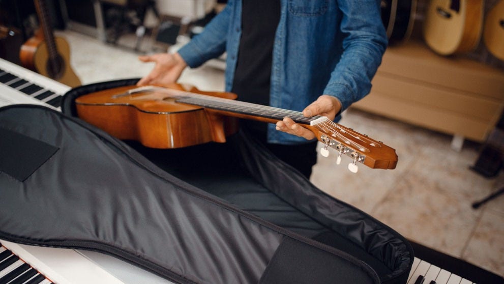 man putting an acoustic guitar into its holding case