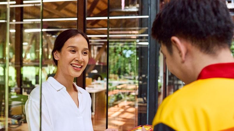 a female customer smiles at a dhl express staff while signing for a delivery on a scanner