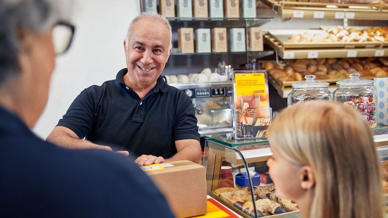 An older man is smiling at two customers he is serving