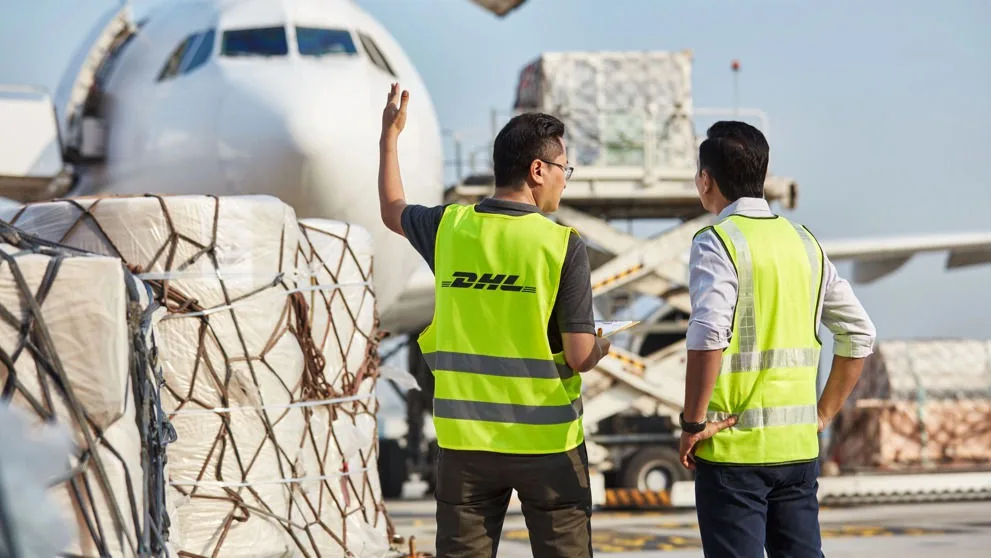 两名 DHL 工作人员在机场停机坪，指挥货机货物装卸作业。