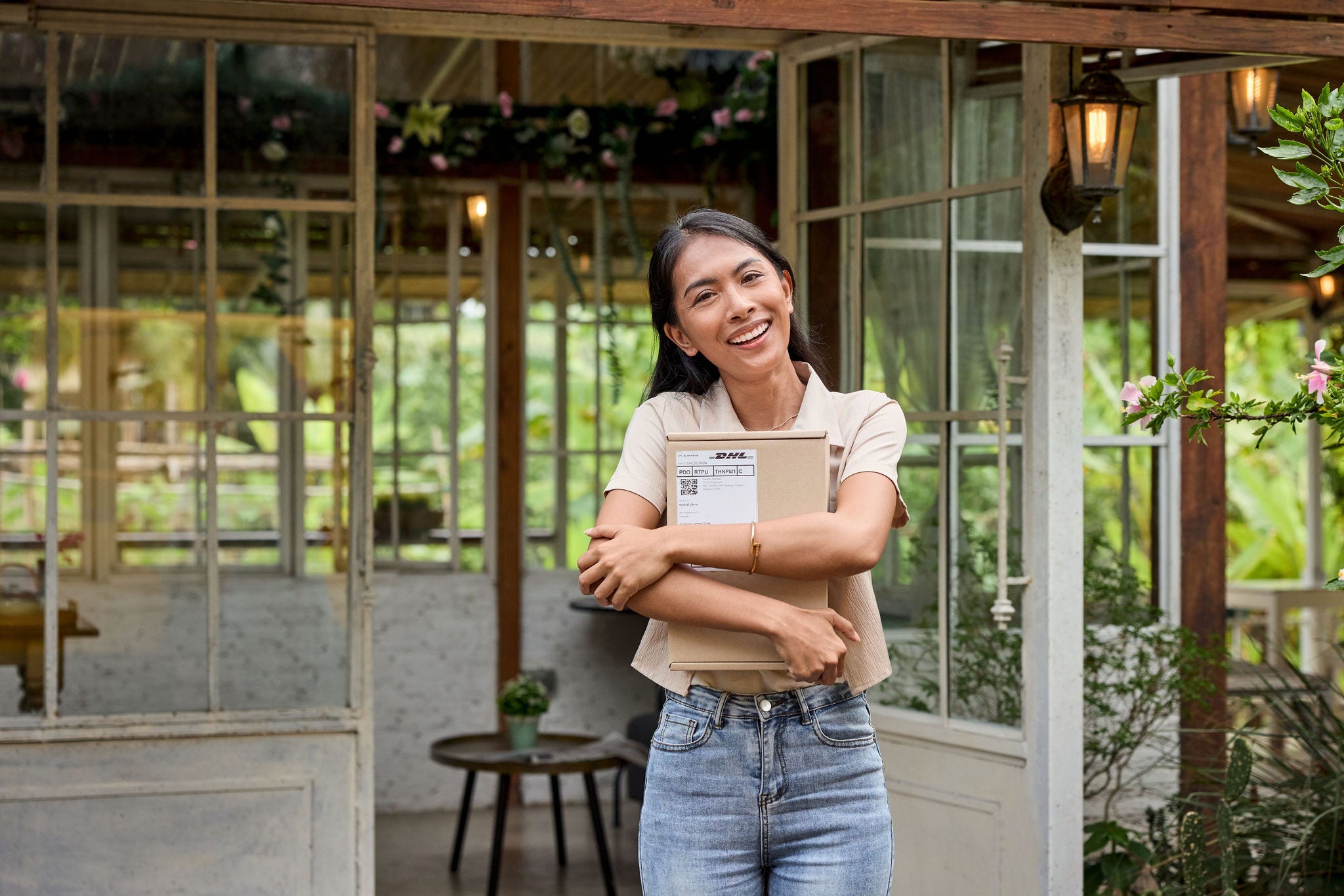 A female customer stands in front of the entrance to her house, smiling and holding a parcel.