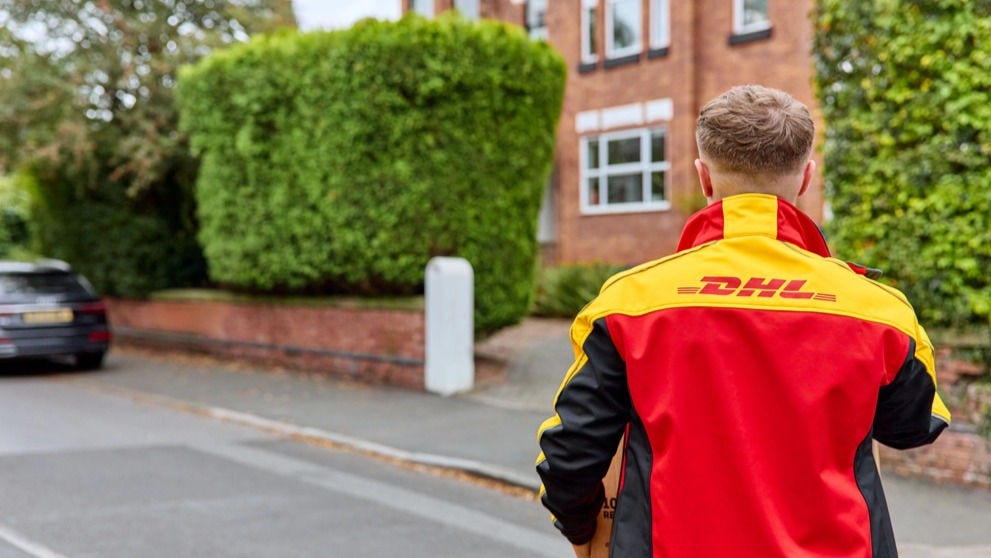 一名 DHL 快递员拎着棕色 DHL 快件，走向联排住宅。