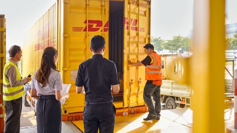 a dhl employee closes a freight container while a male dhl expert and two customs officers inspect it