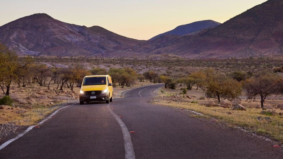 A DHL Express van making its way through a steppe landscape with mountains in the background.