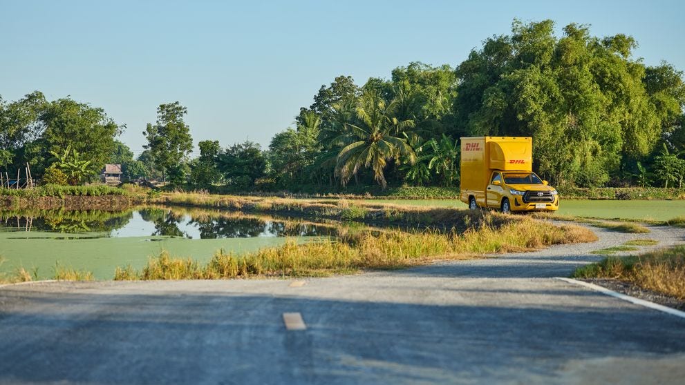 DHL truck driving through a narrow Southeast Asian countryside road.