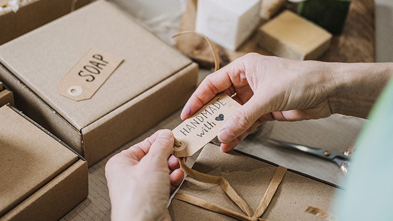 Hands attaching a handmade tag to a kraft gift box beside soap bars