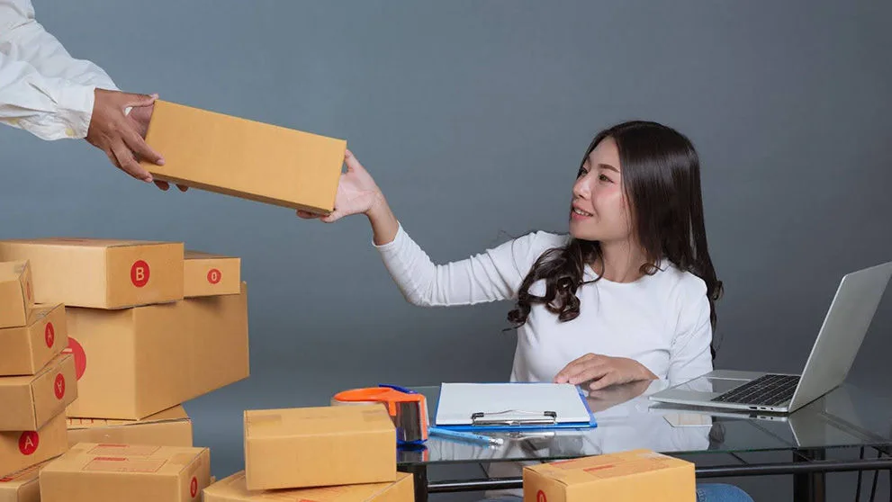 A businesswoman with a laptop passing one of many parcels to a colleague for her dropship business