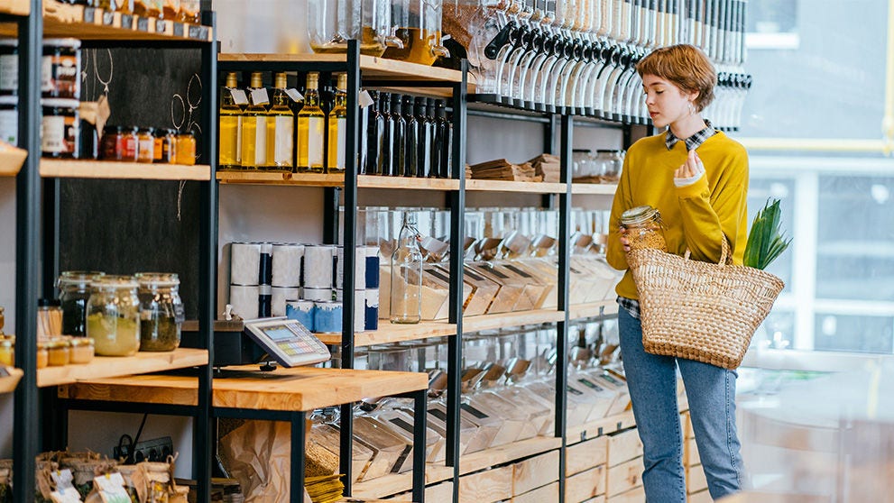 Jeune femme caucasienne achetant des superaliments dans une boutique zéro déchet. Beaucoup de nourriture saine dans des bouteilles en verre sur un stand au supermarché. 