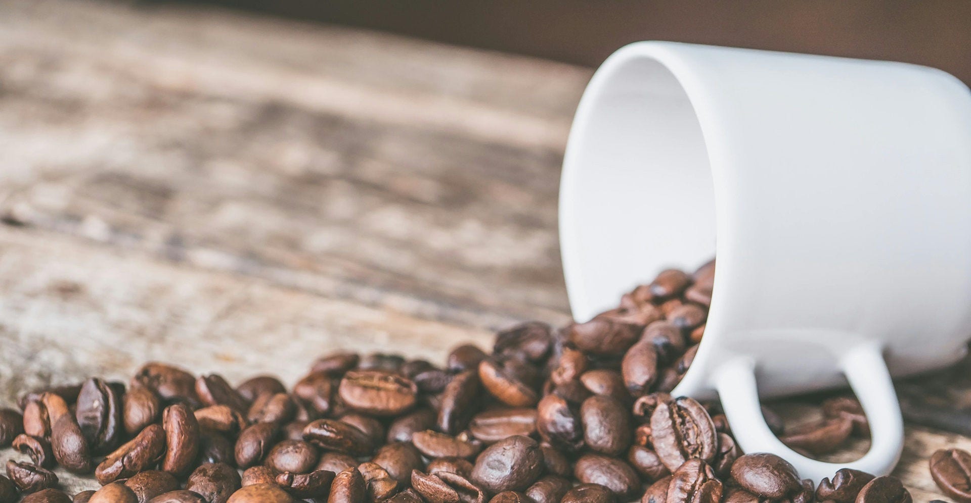 Coffee beans spilling out of a white mug.