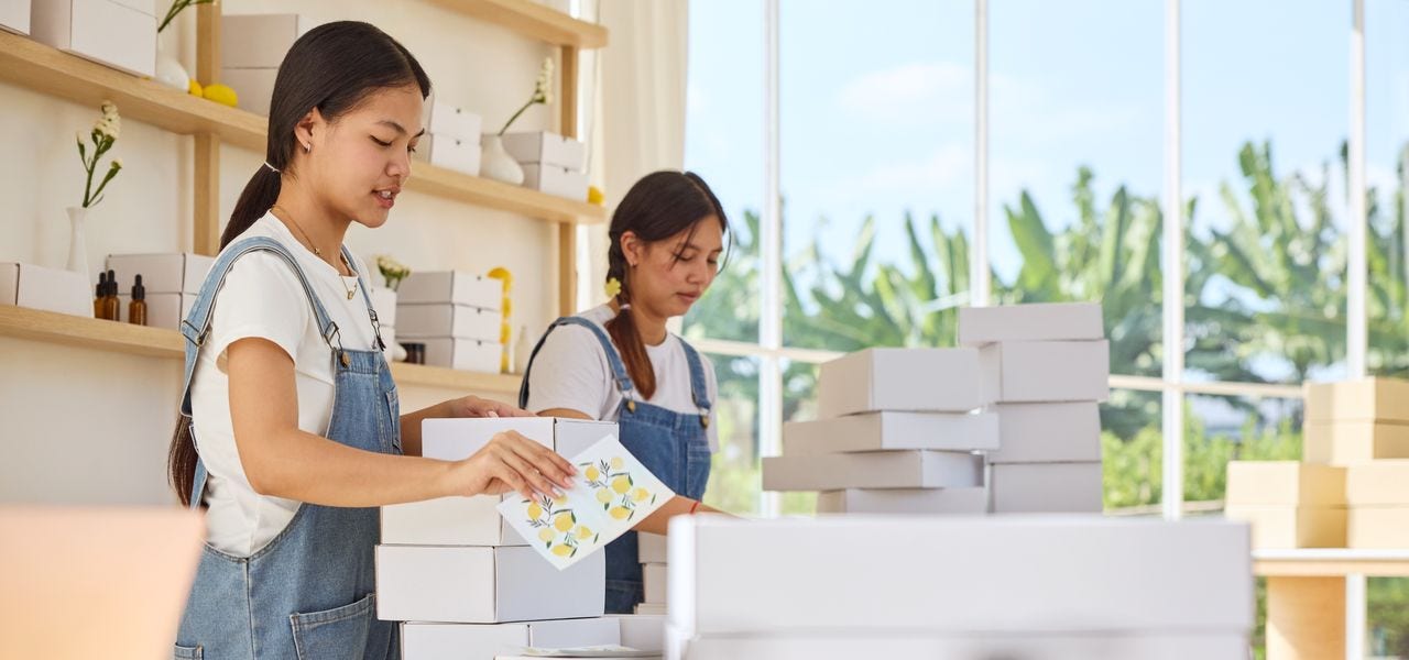 Two young female shop employees are preparing white parcels for shipment.