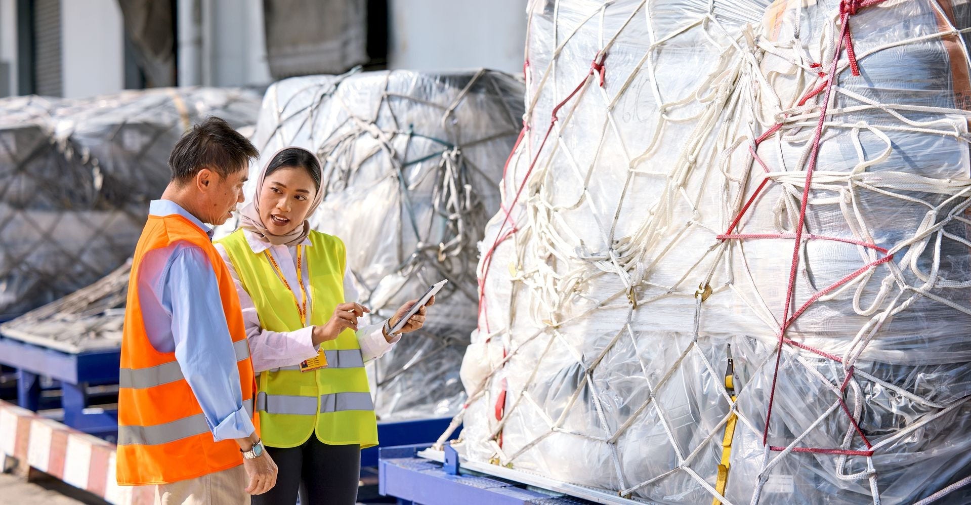 a female dhl expert with tablet in her hand and a male business customer having a conversation about shipping options at an airfield.