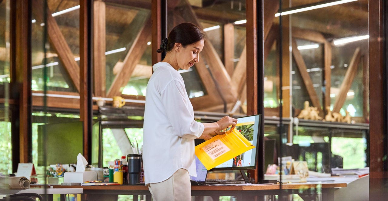 A woman opens an express envelope while standing in front of a desk. 