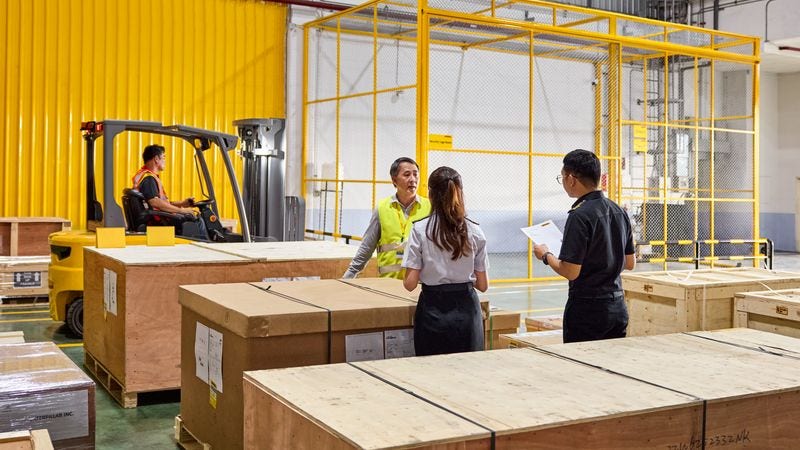 DHL staff discuss while surrounded by big parcels for delivery