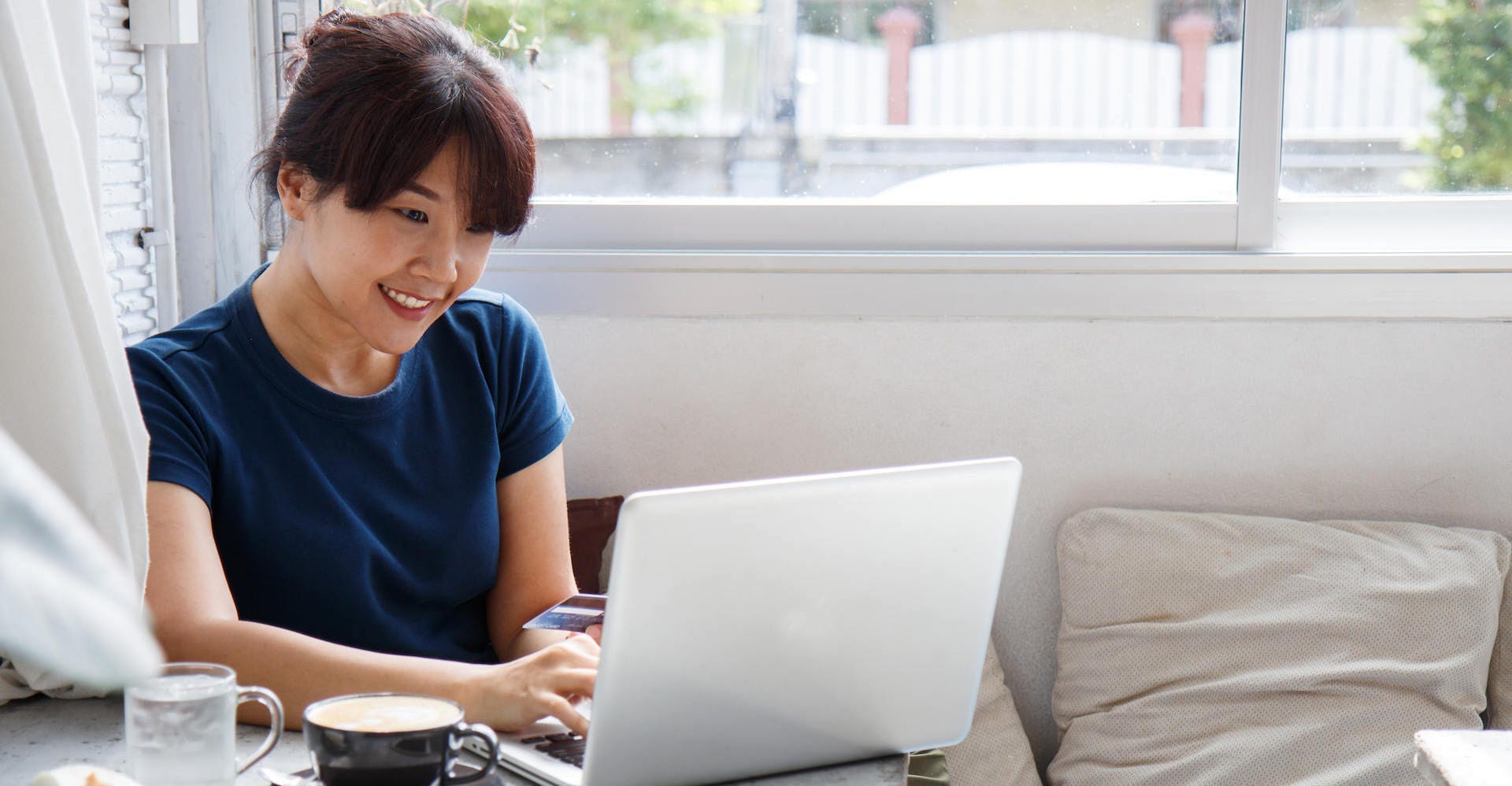 Asian young woman holding credit card mockup and using laptop computer while sitting in cafe. Online shopping concept. Copy space. Selective focus.; Shutterstock ID 1208092774; Purchase Order: -