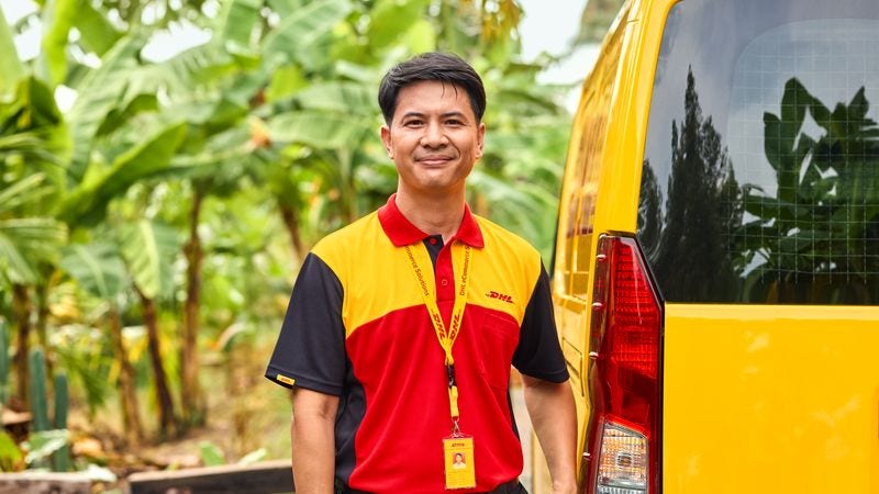 Karyawan DHL berdiri di samping van perusahaan.