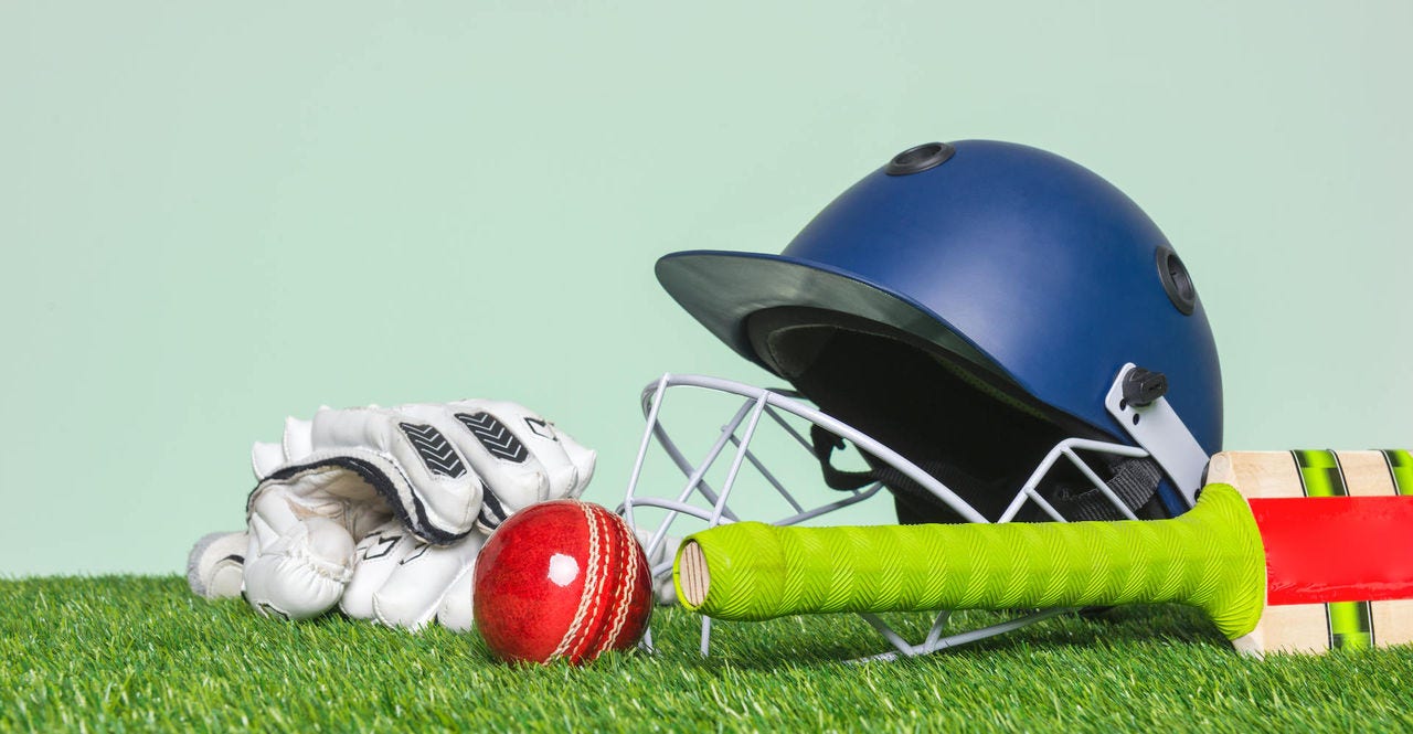 Cricket equipment with bat, ball, helmet and gloves on grass with green background.